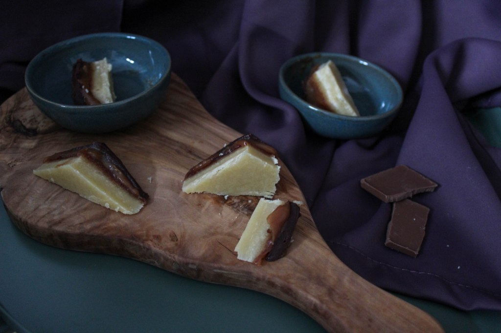 Mehrere Stücke Millionaire's Shortbread auf einem Brett und in Schüsseln. Zu sehen sind die verschiedenen Schichten von Mürbeteig, Karamell und Schokoladenganache.